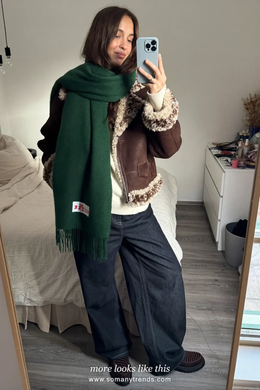 Brown sheepskin jacket with green scarf, wide dark jeans and boots on a snowy street, outfit 8