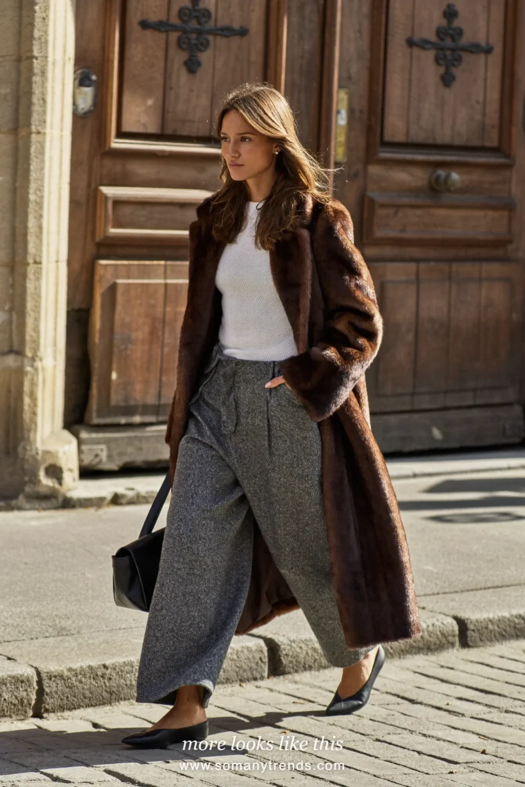 Long chocolate brown faux fur coat over a white knit top, gray tailored wide-leg pants and black pointed flats, outfit 1