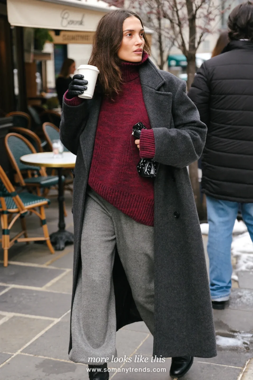 Woman in burgundy oversized knit sweater, gray wide-leg wool pants, gray long coat over arm area, black ankle boots, look 3