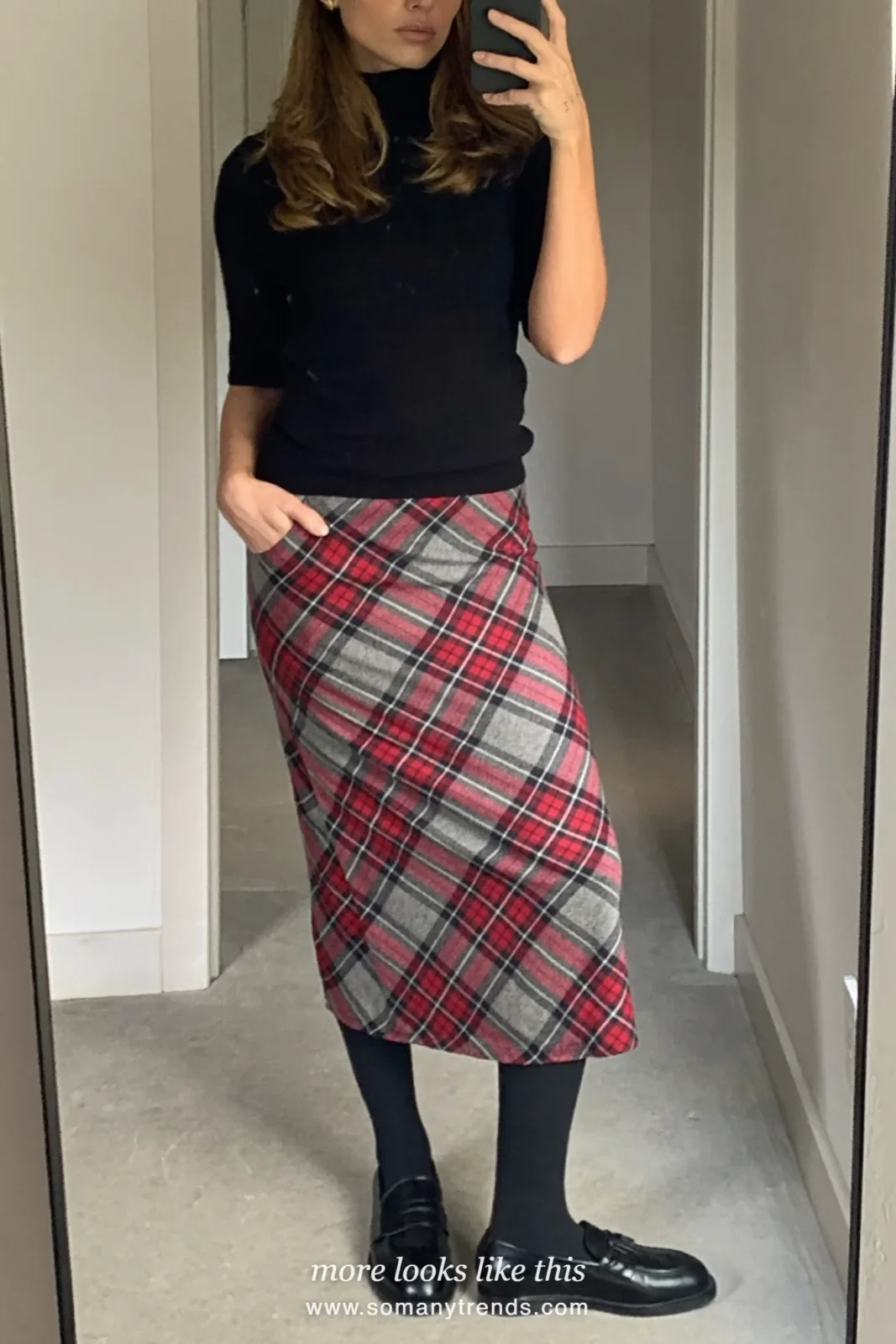Woman in black fitted turtleneck, red and gray tartan wool midi skirt, black sheer tights and black loafers, mirror selfie at home, look 4