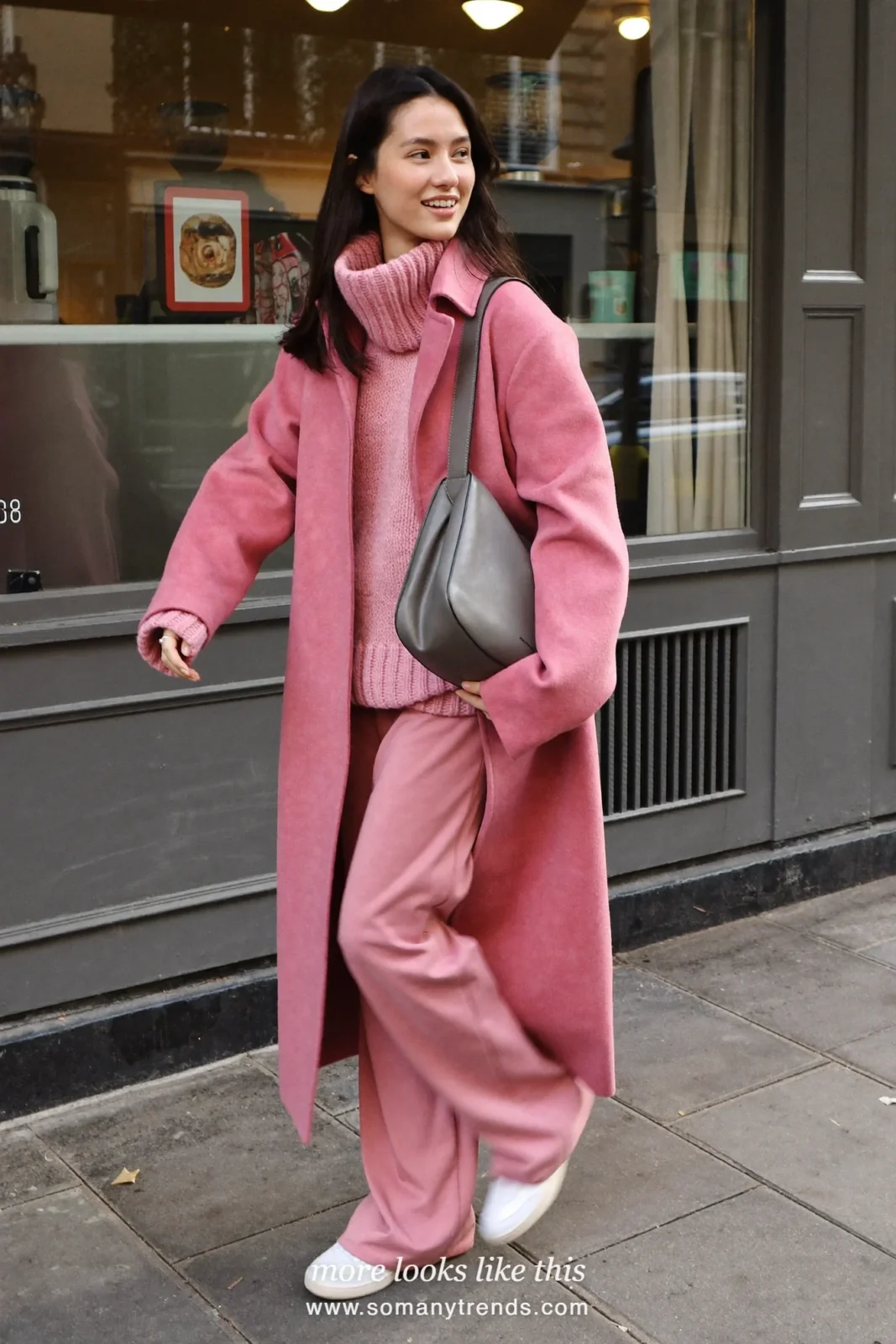 Woman in dusty pink long wool coat over dusty pink knit sweater, pink wide-leg pants, gray bag and white sneakers, look 7