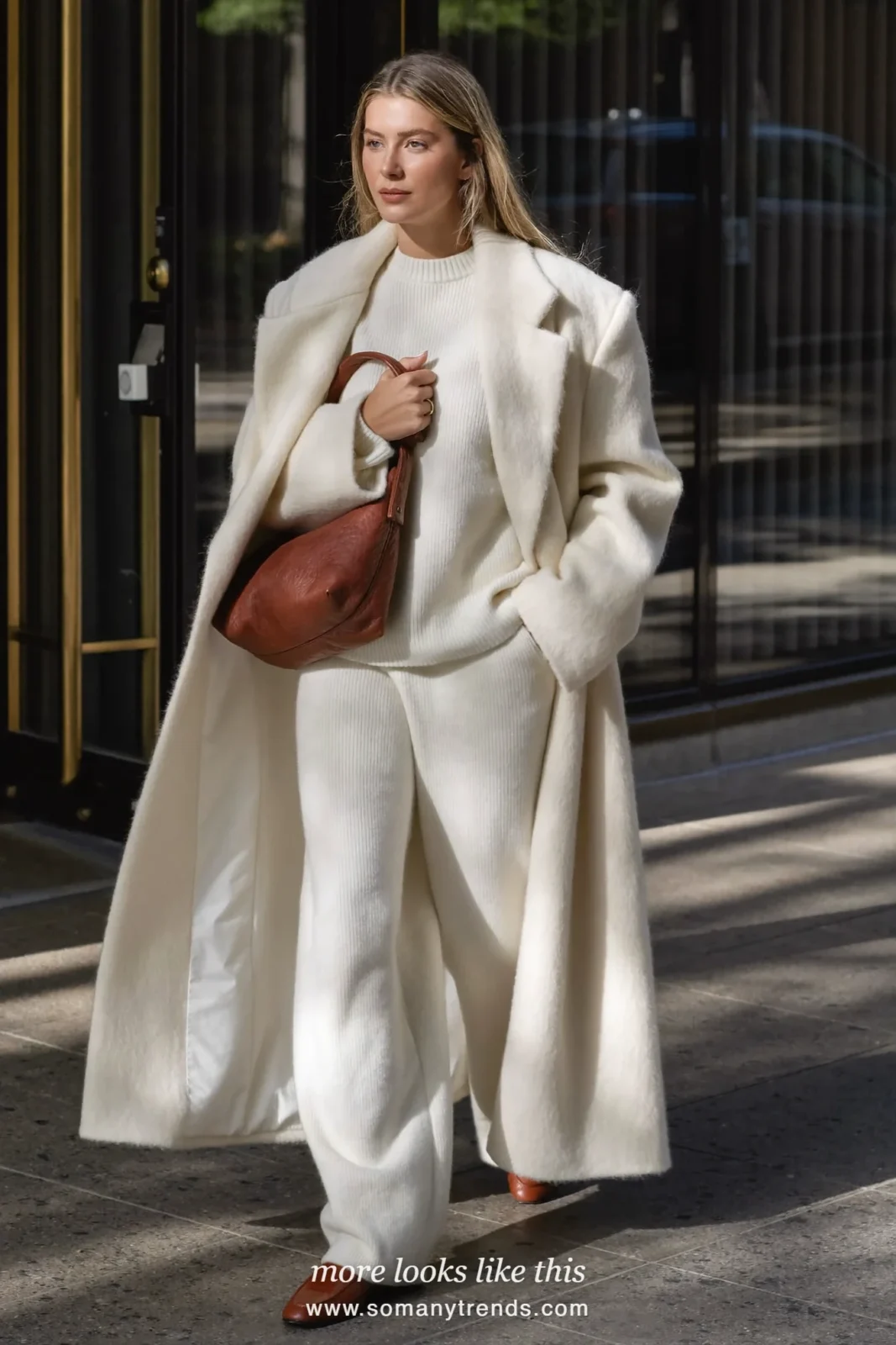 Woman in cream ribbed knit, cream wide-leg pants, cream long wool coat, brown leather bag and brown loafers, look 13