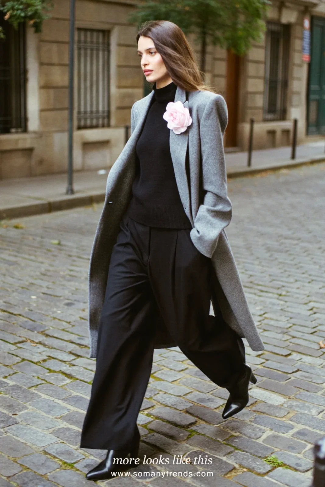 Woman in gray long wool coat with 3D fabric flower on lapel, black turtleneck, black pants and black ankle boots, look 15
