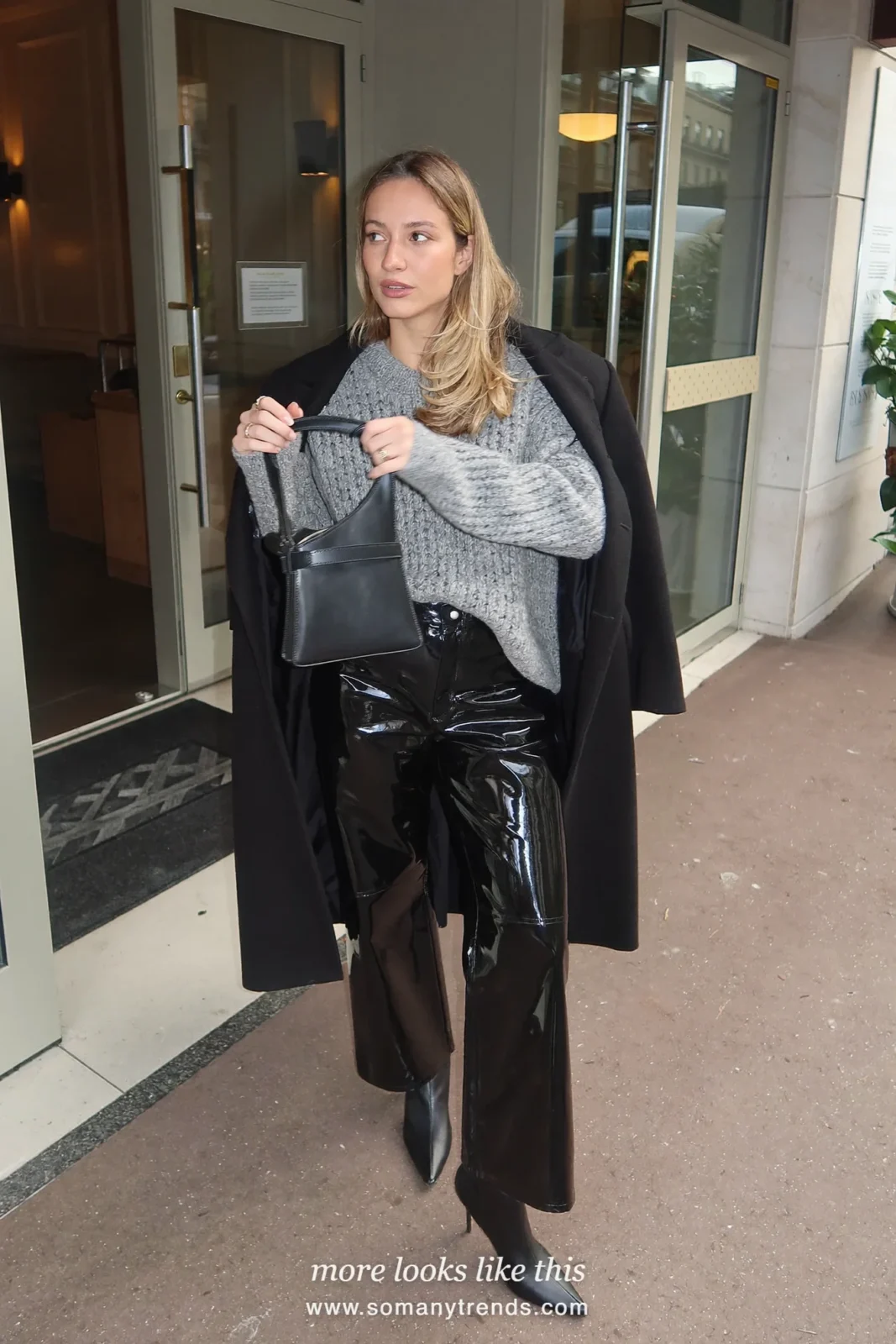 Woman in black glossy wide-leg vinyl pants, gray chunky knit sweater, black pointed boots and black coat, look 18