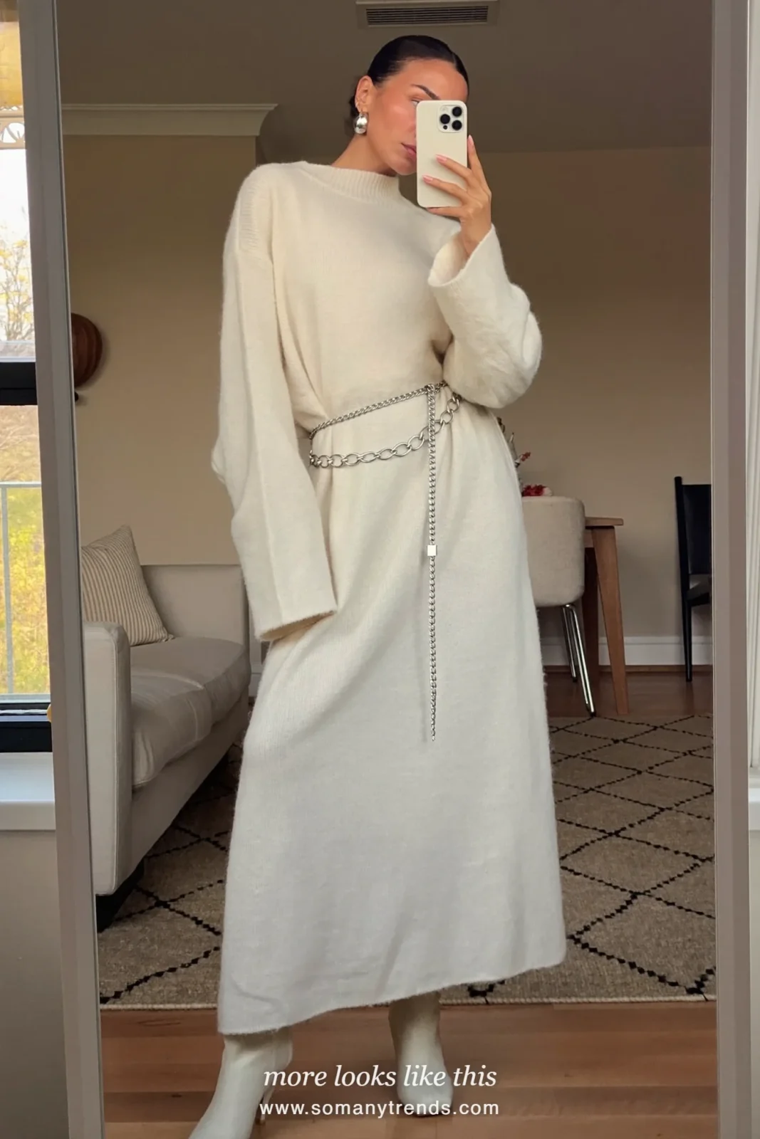 Woman in ivory loose knit maxi dress with silver earrings and ivory ankle boots taking a mirror selfie, outfit 12