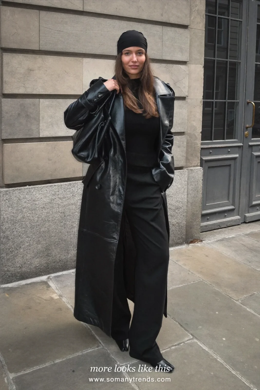 Woman in a long black leather trench, black wide-leg pants, black head wrap and black boots on a city street, outfit 1