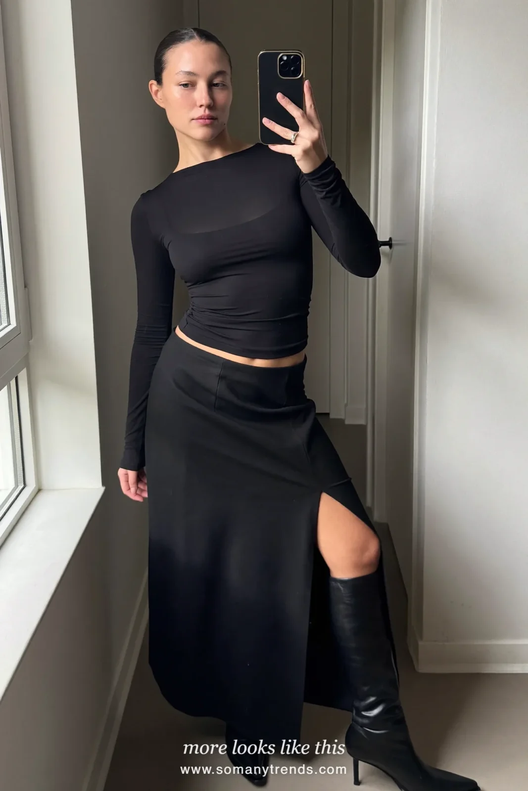 Woman taking a mirror selfie in a black fitted top, black maxi skirt and black leather boots at home, outfit 4