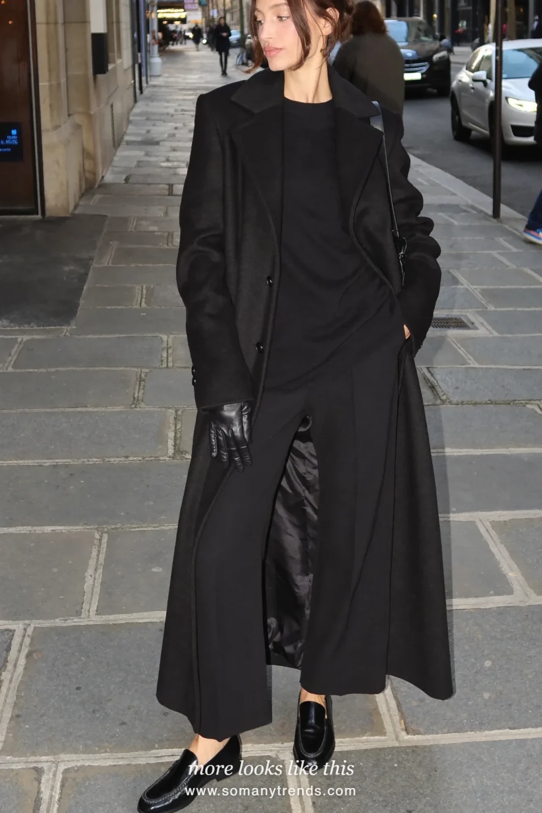 Woman in a long black wool coat, black knit, black pants and black leather gloves on a stone street, outfit 5