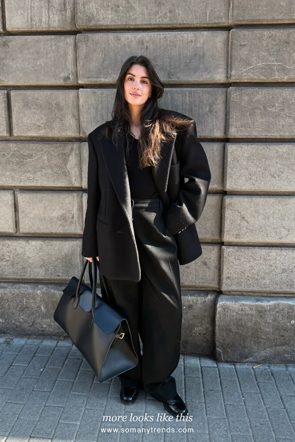 Woman in an oversized black blazer, black knit top, wide-leg black pants and black loafers outside a stone facade, outfit 9