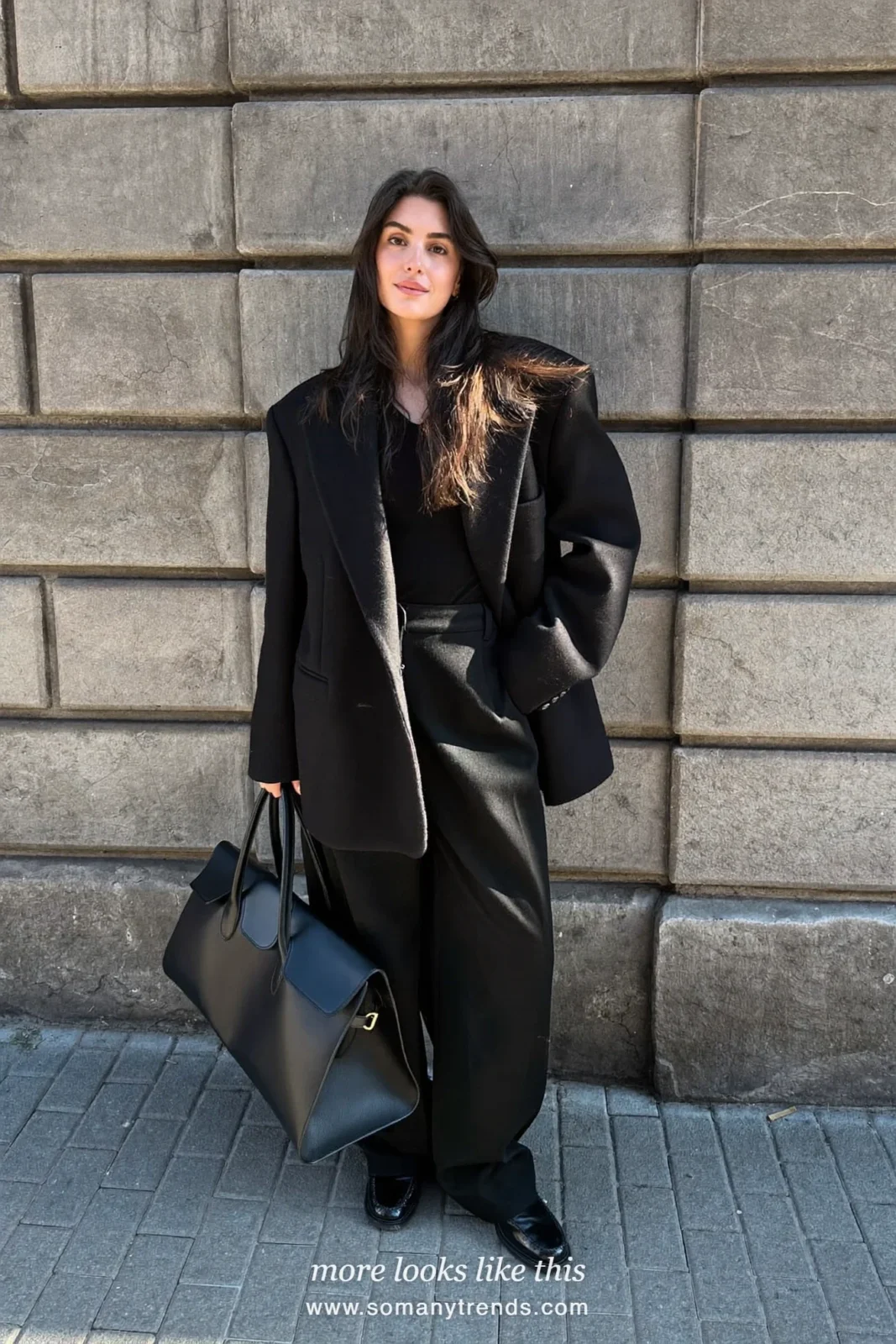 Woman in an oversized black blazer, black knit top, wide-leg black pants and black loafers outside a stone facade, outfit 9