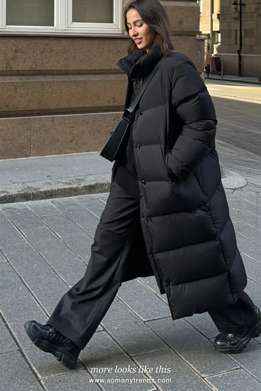 Woman in a long black puffer coat, black knit hat, wide black pants and black sneakers on a city street, outfit 18
