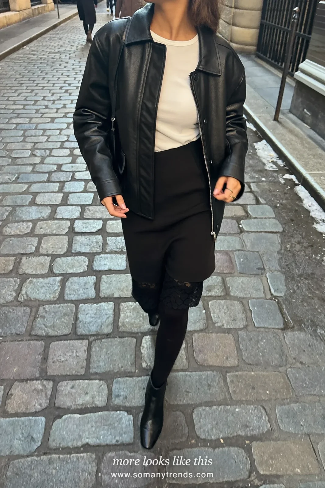 Woman in a black leather jacket, white tee, black lace hem skirt, tights and boots on a city street, outfit 19