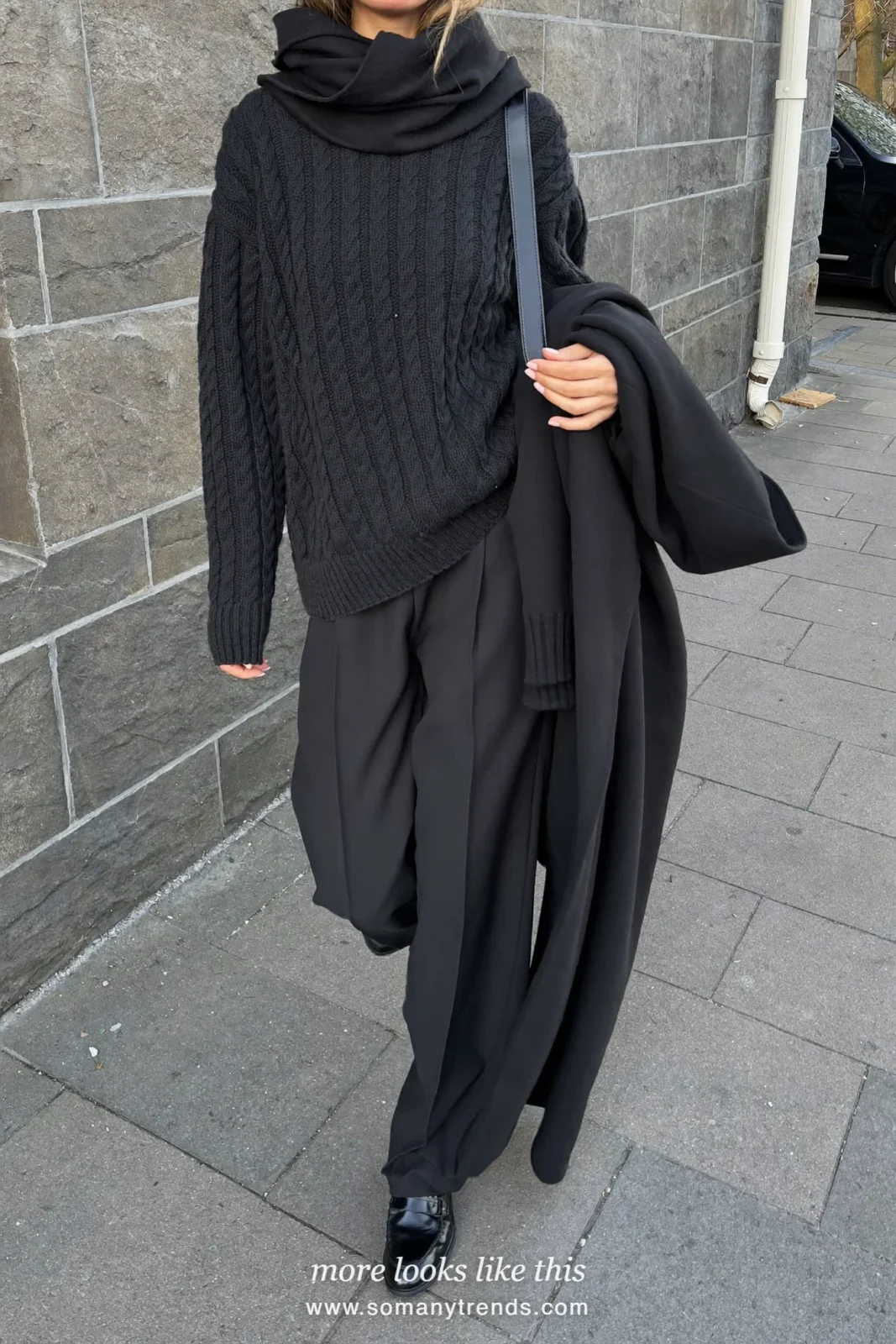 Woman in a black cable-knit sweater, black wool pants and black loafers on a city street, outfit 25