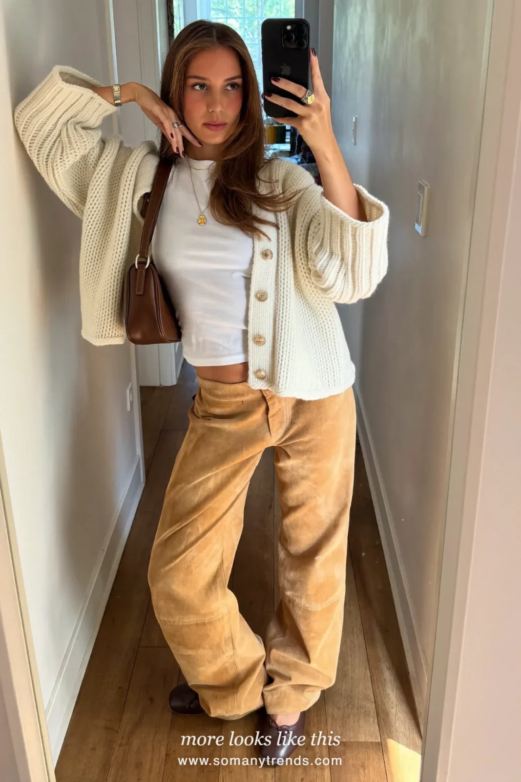 Woman in tan suede wide-leg pants, cream cardigan, white tee and brown flats taking a mirror selfie in a hallway, outfit 4
