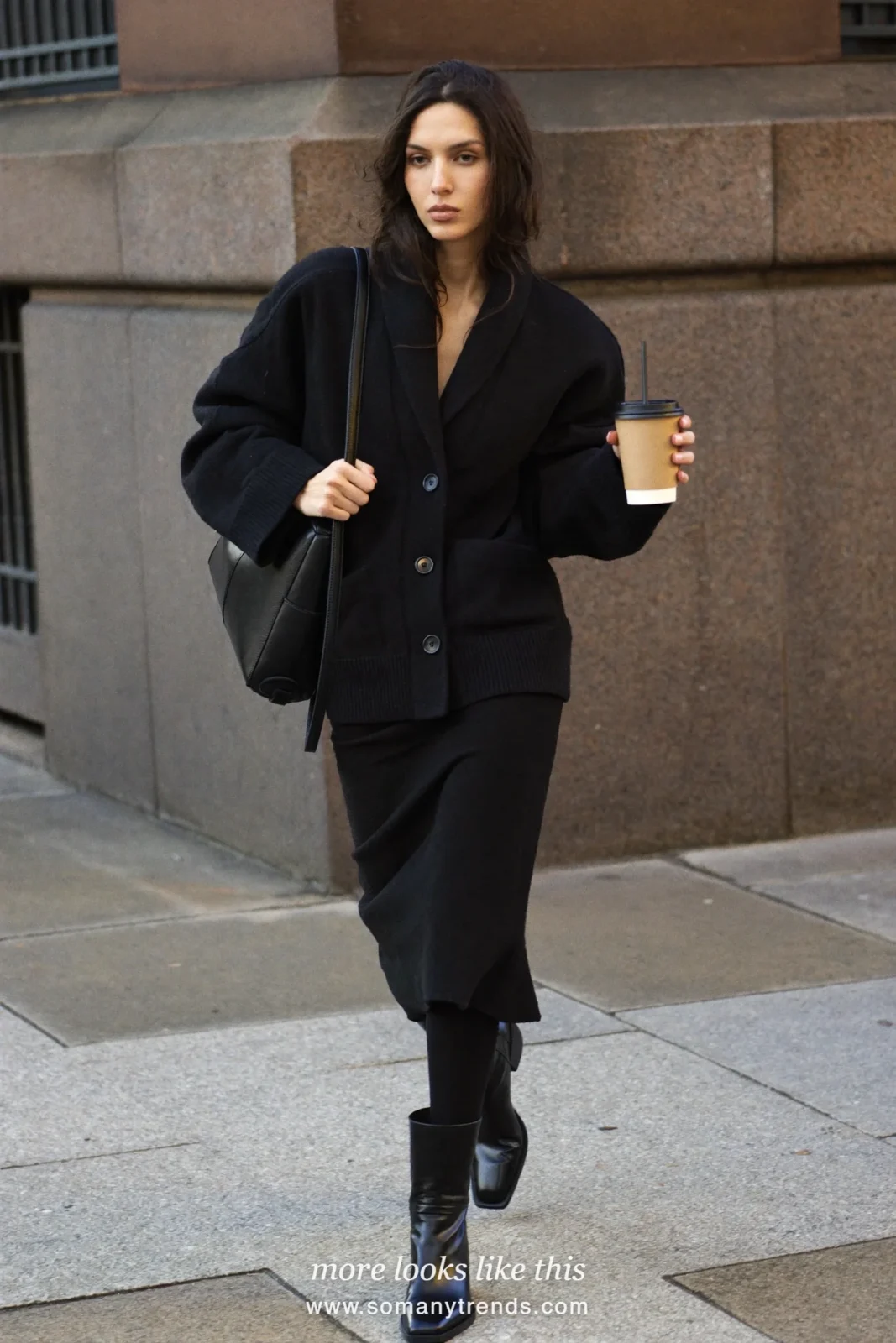 Woman in a black wool midi skirt, oversized black cardigan, black tights and boots on a city street, outfit 17