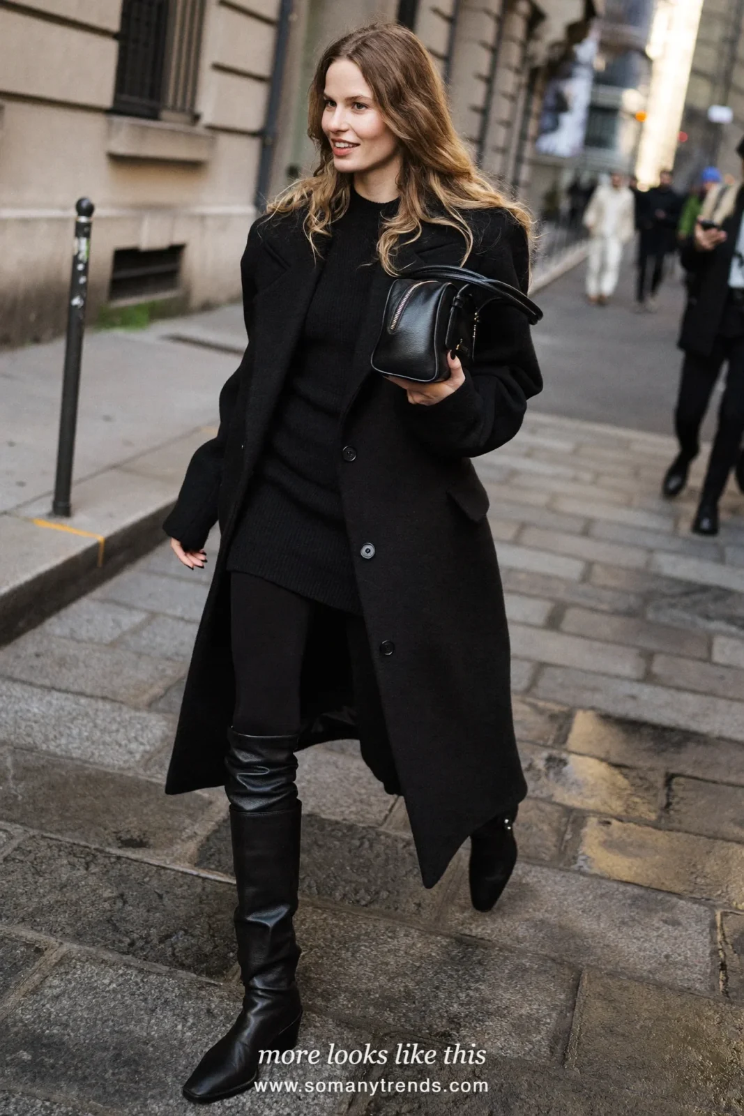 Woman in a long black coat over a ribbed knit mini, black tights and tall boots on a city street, outfit 21