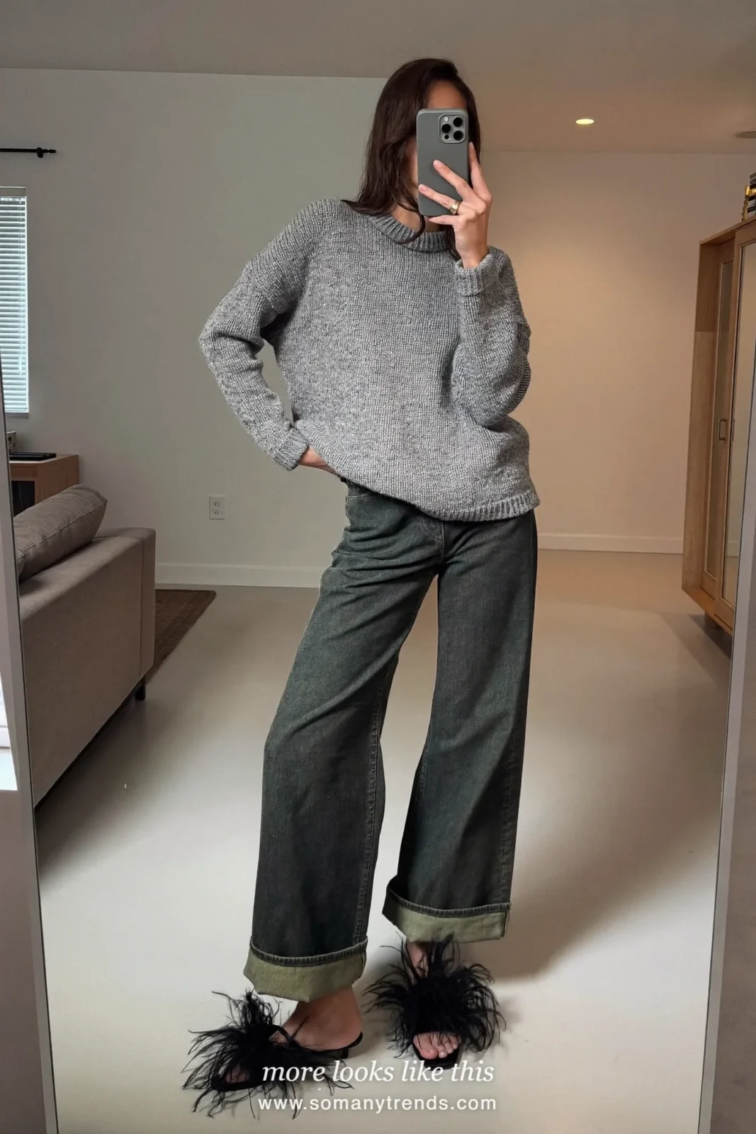 Woman taking a mirror selfie in a gray knit sweater and dark green wide cuffed jeans with feathered shoes in a Paris apartment living room, outfit 4