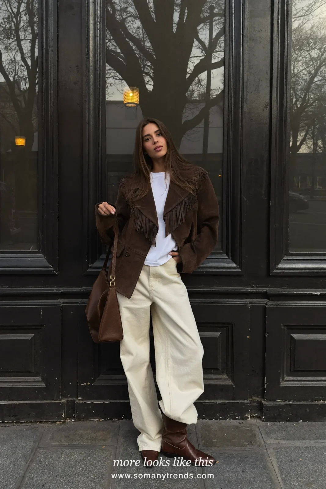 Woman in a chocolate brown suede fringe jacket, cream jeans and brown western ankle boots on a Paris street, outfit 11
