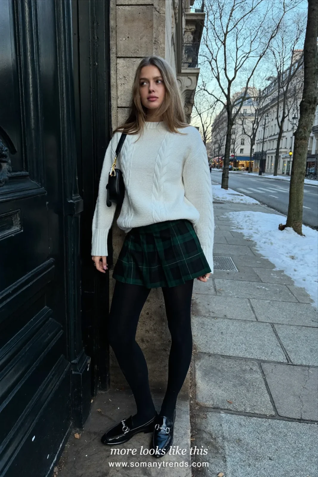 Woman in a cream cable knit sweater, green tartan pleated mini skirt, black tights and loafers on a Paris street, outfit 14