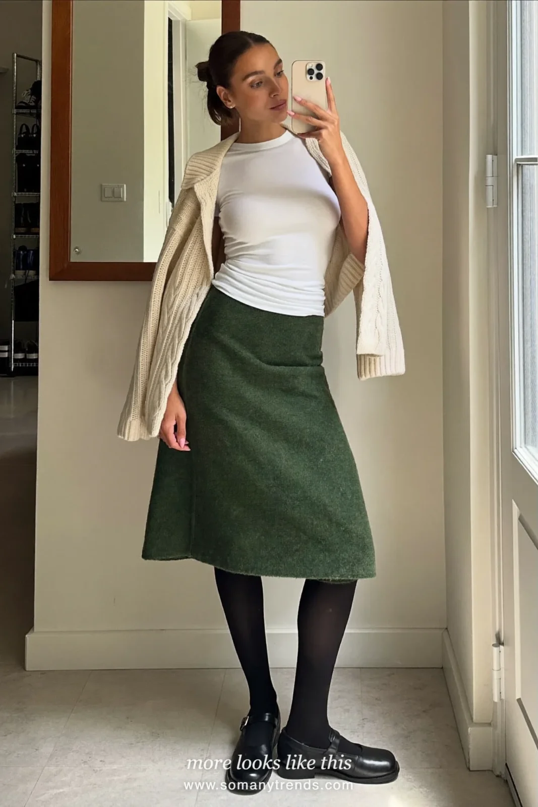 Woman in a cream cardigan, bottle green wool midi skirt, black tights and mary janes on a Paris street, outfit 16