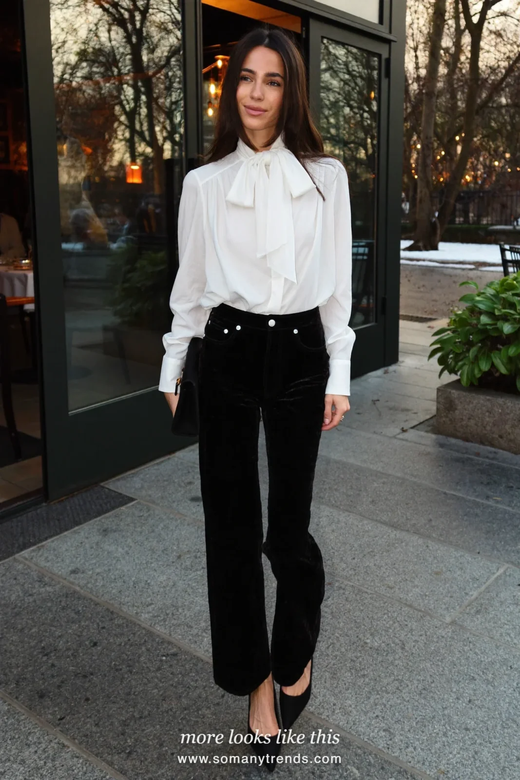 Woman in black velvet wide pants, white bow blouse and pointed black pumps at a Paris restaurant entrance, outfit 26