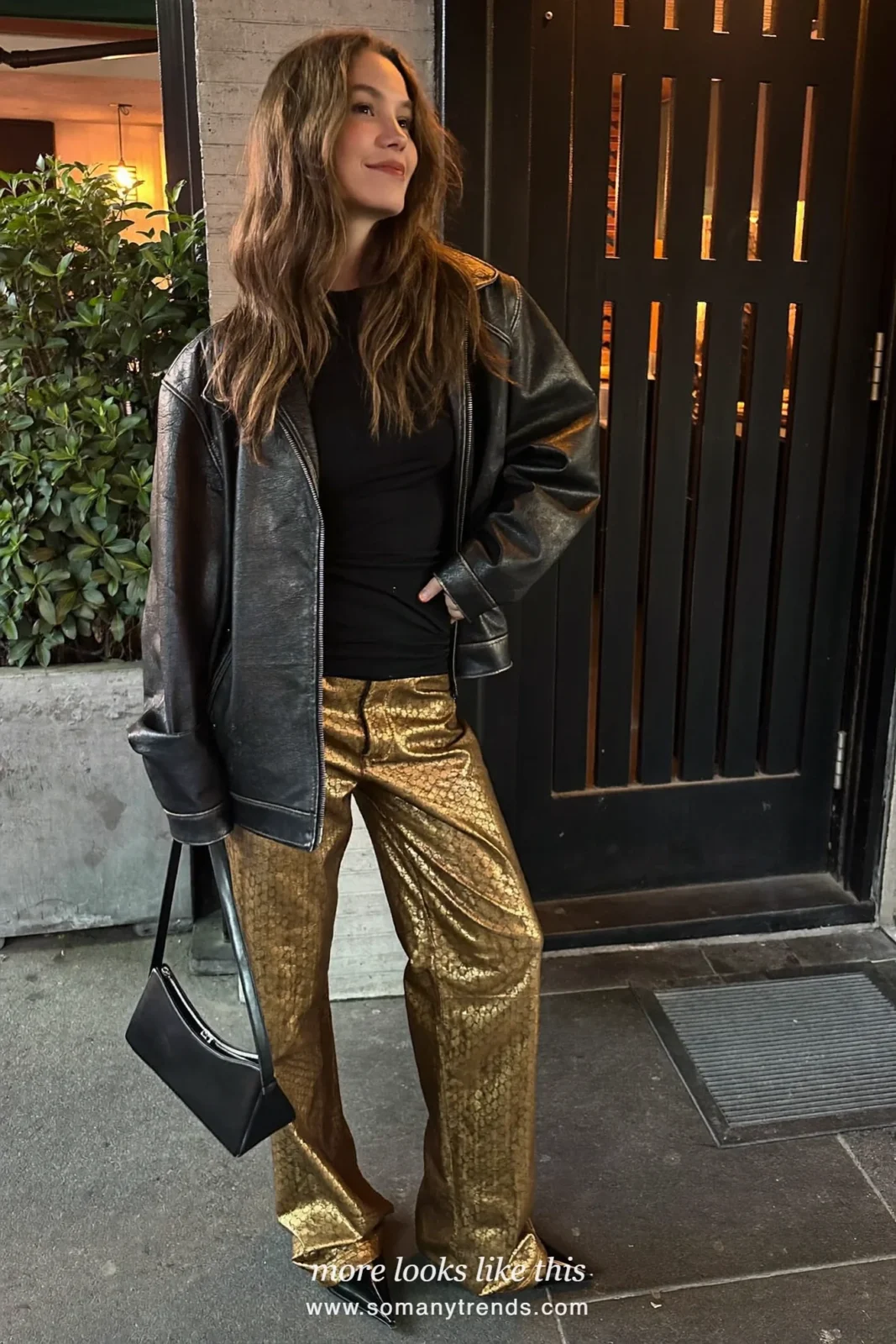 Woman in a black leather jacket, black top, gold patterned metallic wide-leg pants and black pointed boots outside a bar at night, outfit 5