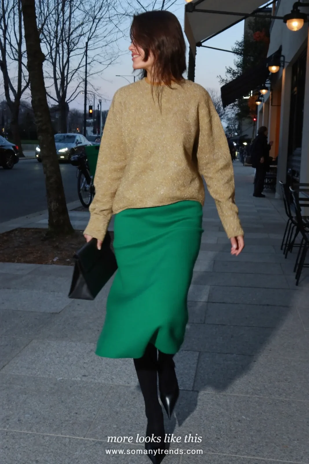 Woman in a gold lurex knit sweater, emerald green midi skirt, black tights and black pumps outside a restaurant, outfit 11