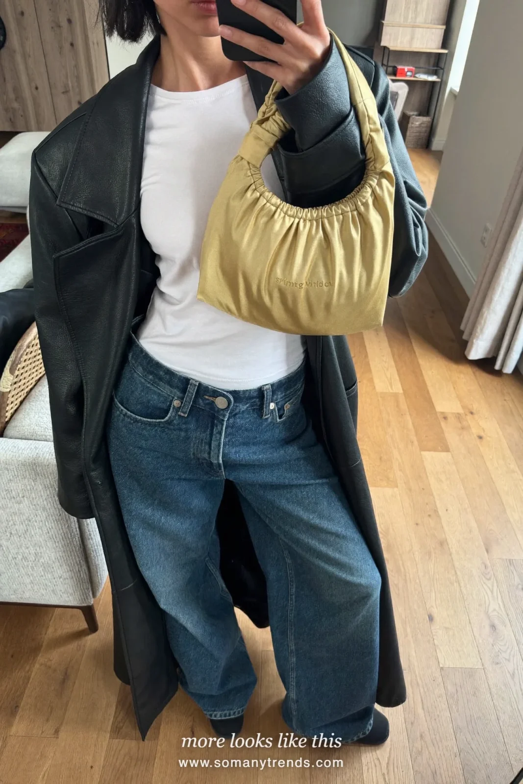 Woman in wide-leg jeans, a white tee, a long black leather coat and a gold satin pouch bag on a staircase, outfit 28