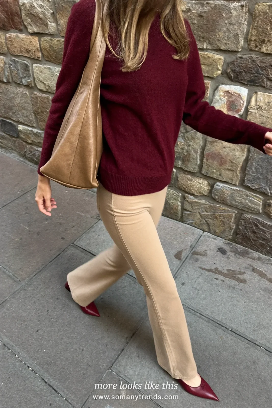 Woman in a burgundy merino sweater, beige flare pants, burgundy pointed flats and a tan bag outdoors, outfit 2