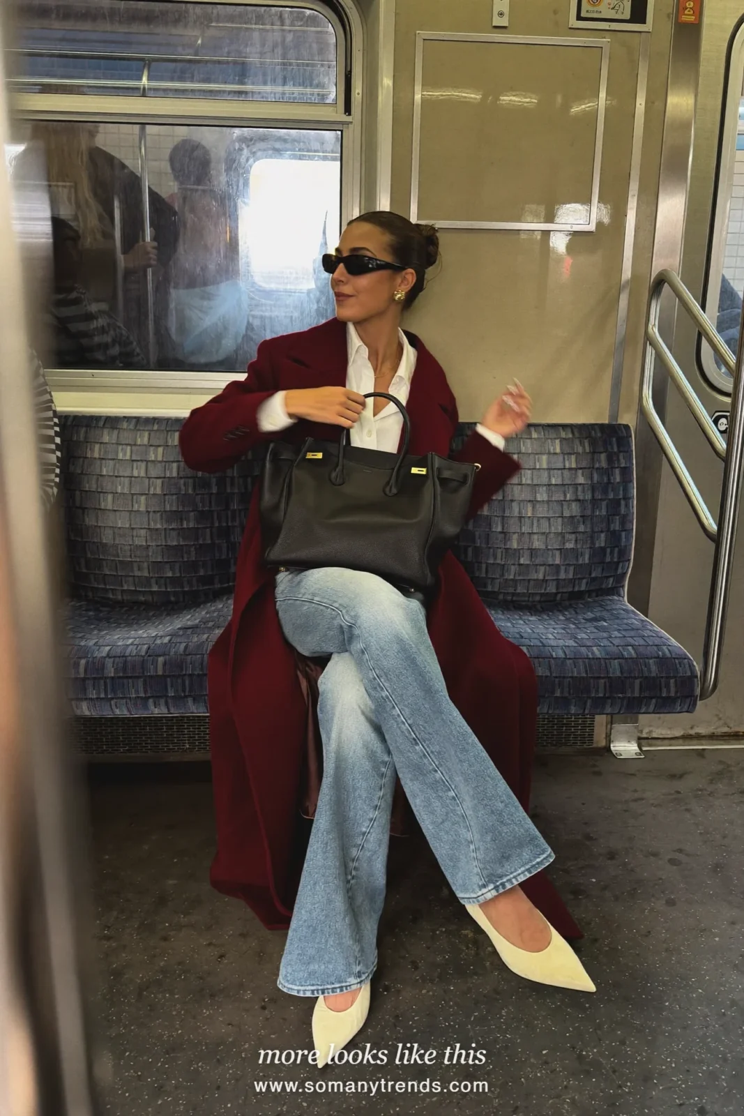 Woman in a long burgundy wool coat, white blouse, light wash flare jeans and cream almond-toe pumps in a subway car, outfit 5