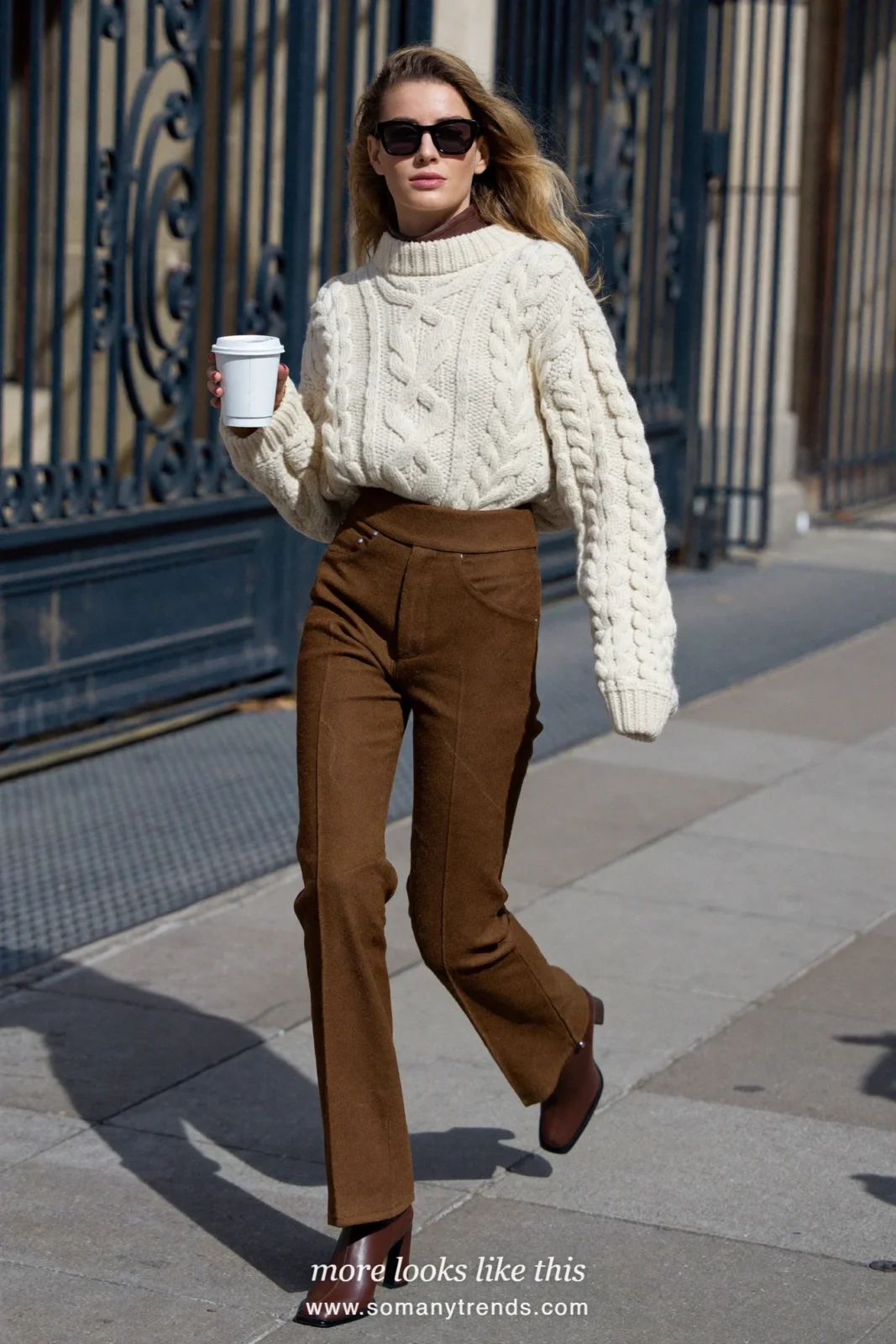 Woman in a cream cable knit sweater, chocolate brown flare pants and brown heeled boots on a city street, outfit 9
