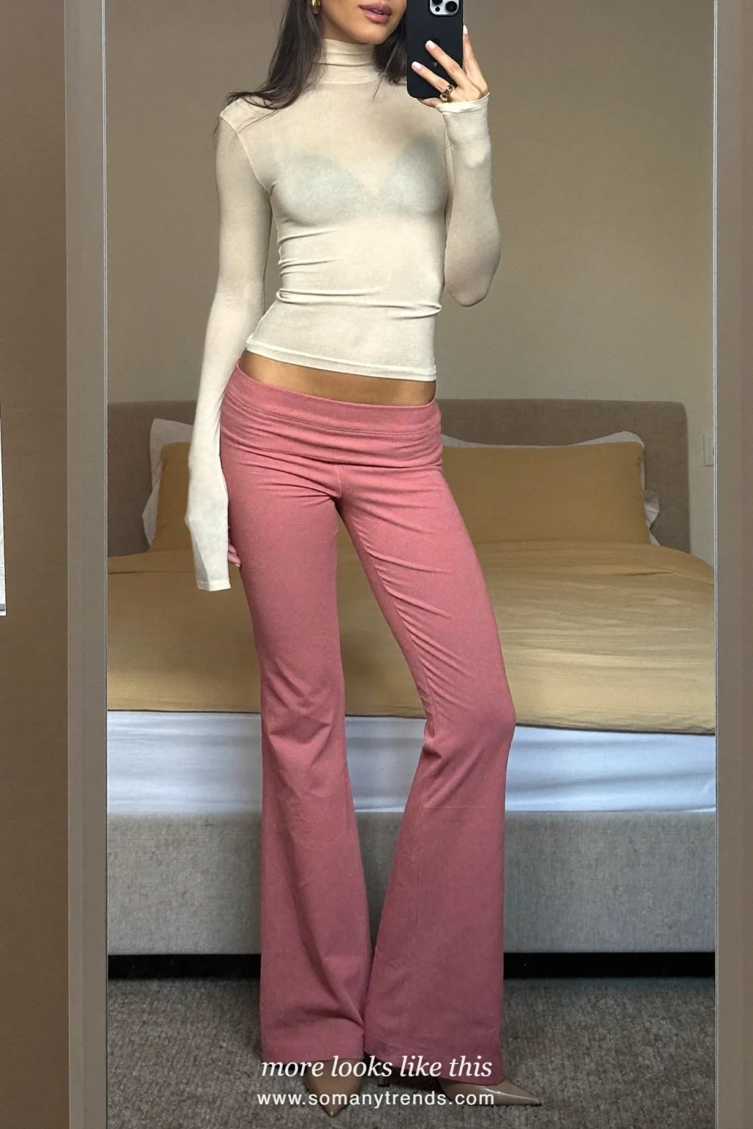 Woman in a cream turtleneck, rose flare pants and nude pumps taking a mirror selfie at home, outfit 12