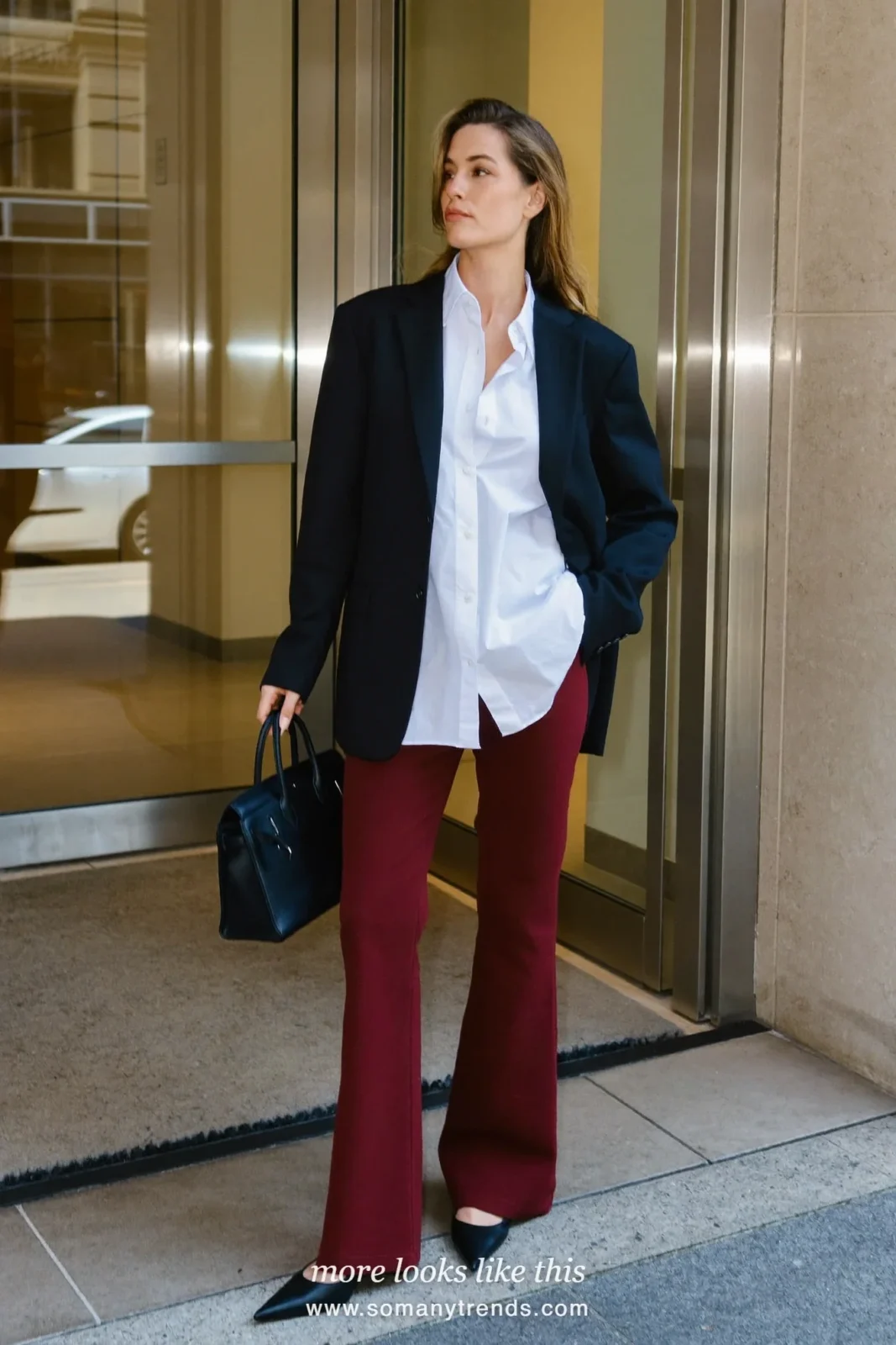 Woman in a black blazer, white shirt, burgundy flare pants and black pointed pumps near an office building, outfit 13