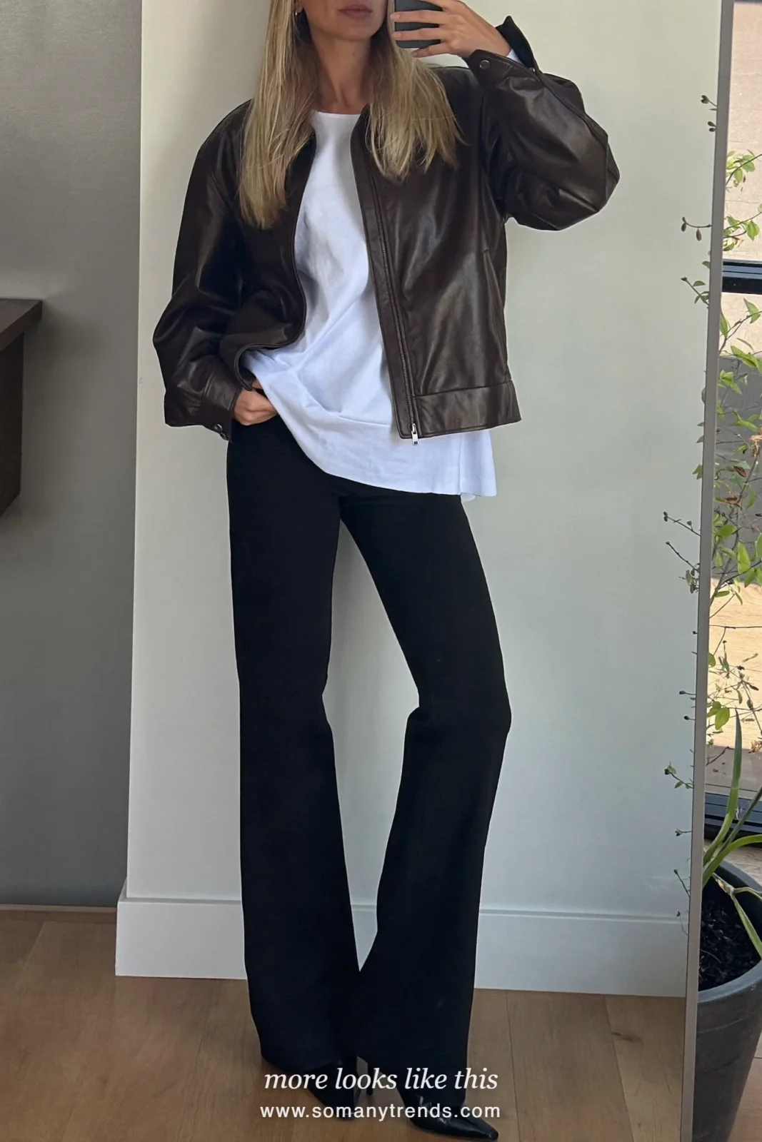 Woman in a chocolate brown leather jacket, white tee, black flare pants and pointed boots taking a mirror selfie, outfit 16