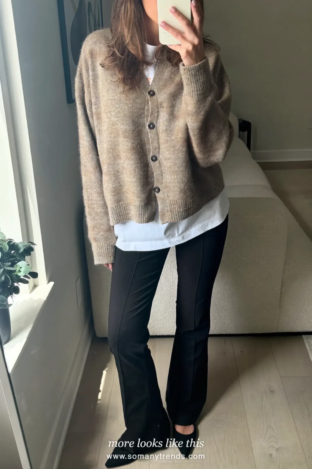 Woman in an oatmeal cardigan, white tee, black flare pants and black pointed flats taking a mirror selfie, outfit 20