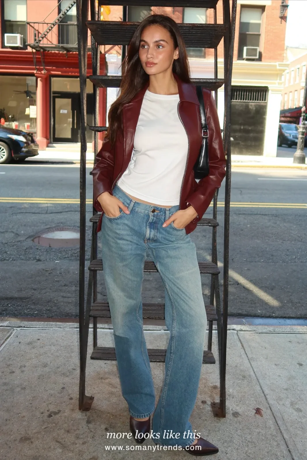 Woman in a burgundy leather jacket, white tee, light flare jeans and chocolate pointed boots on a city street, outfit 21