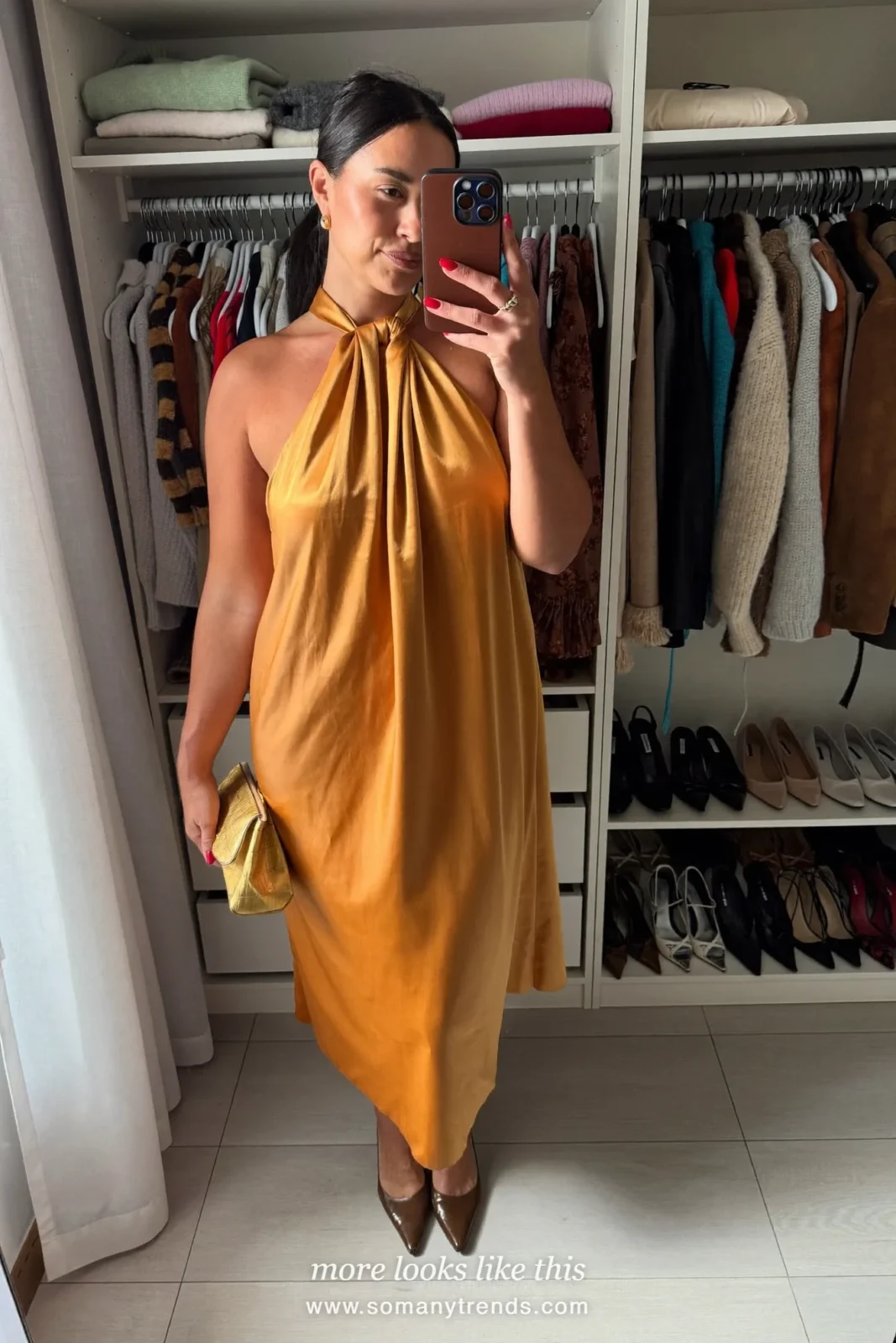Woman in an amber satin halter midi dress with brown heels in a room with a fireplace, outfit 16