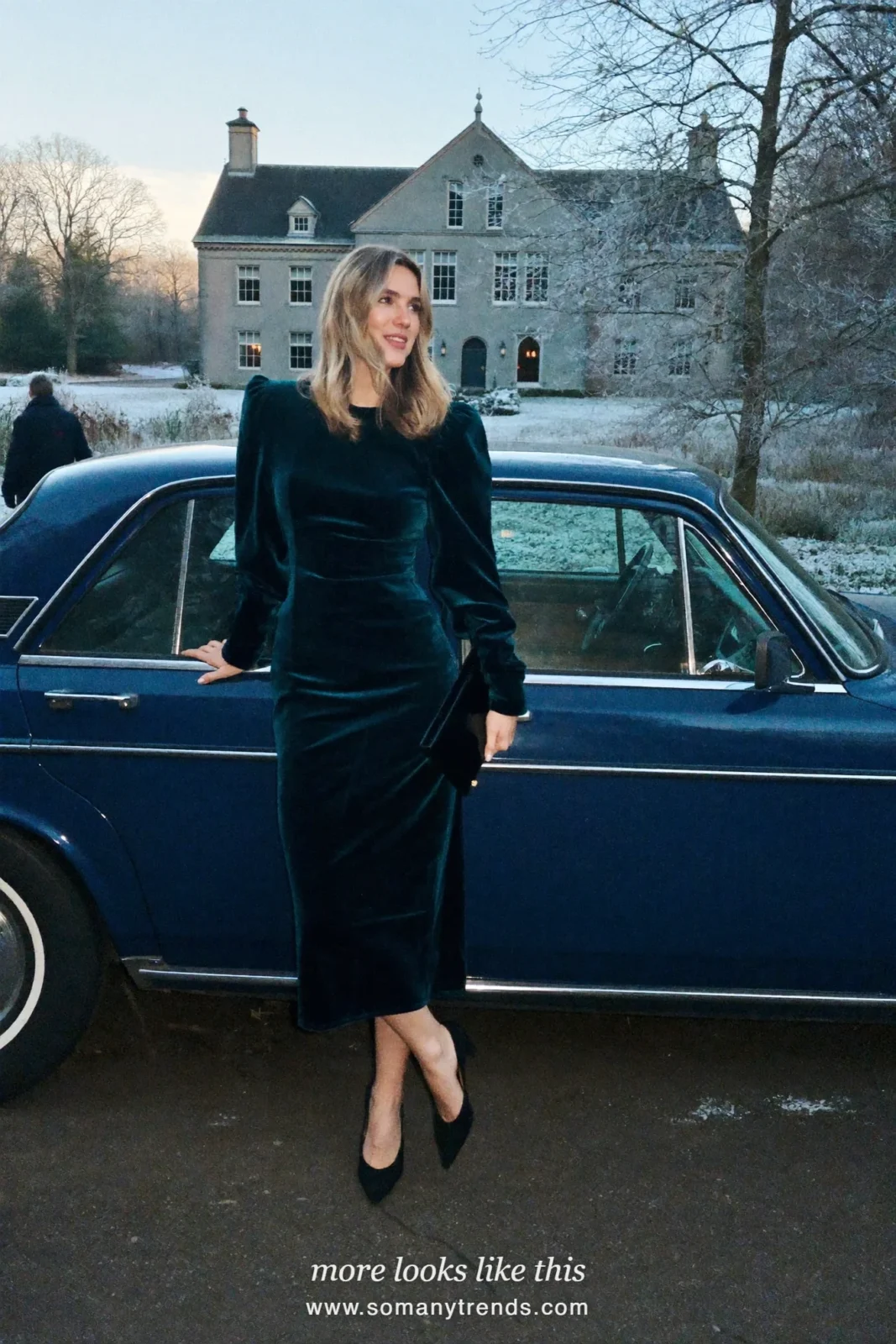 Woman in a dark teal velvet midi dress with puff sleeves and black pumps beside a vintage car at a country manor, outfit 17
