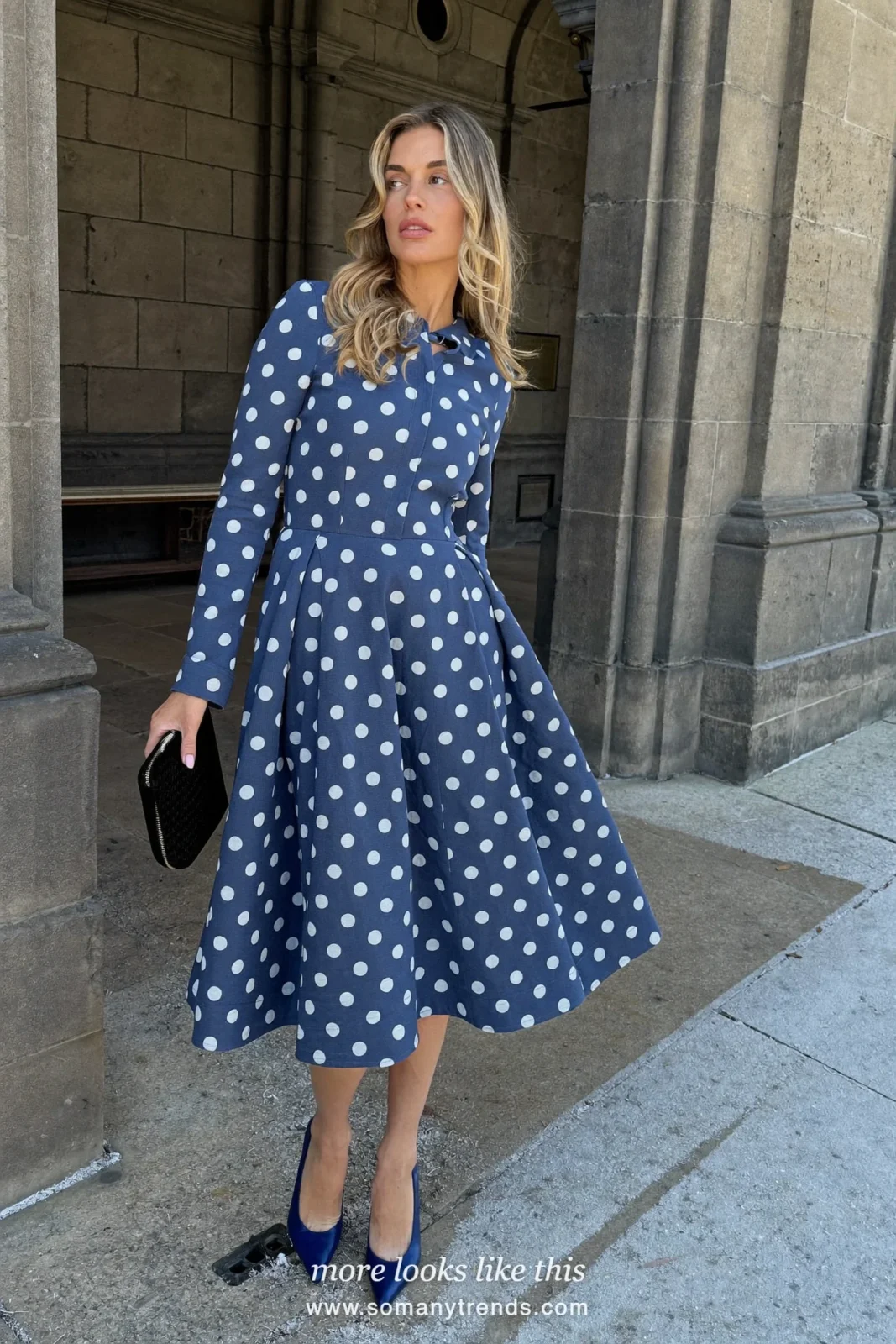 Woman in a sapphire blue polka-dot midi dress with a flared skirt and navy pumps in a stone church doorway, outfit 13