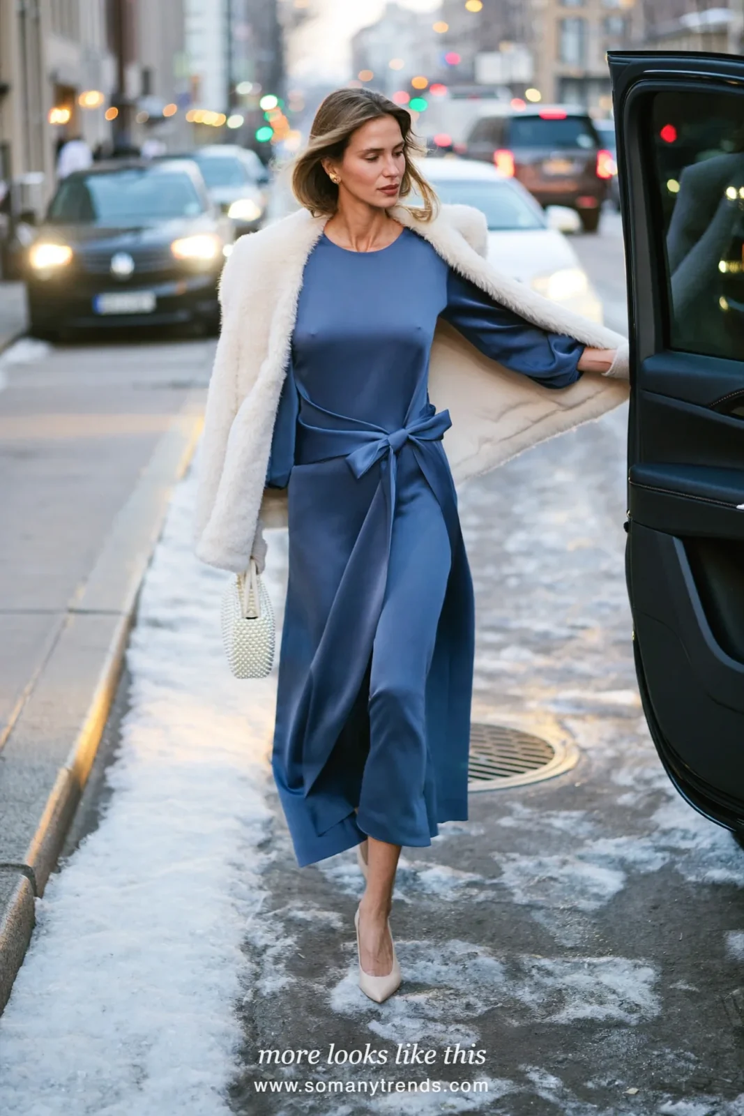 Woman in a dusty blue satin midi dress with a bow at the waist and a cream faux-fur wrap with nude pumps, outfit 22