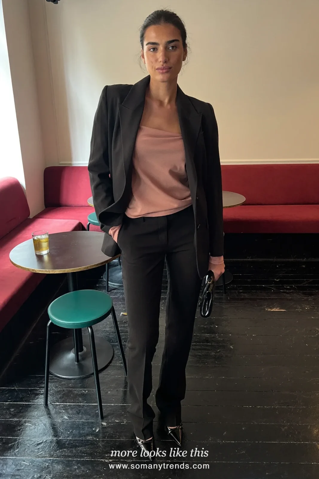 Woman in a rose camisole, black blazer, black flare pants and black pointed heels in a bar with red banquettes, outfit 23