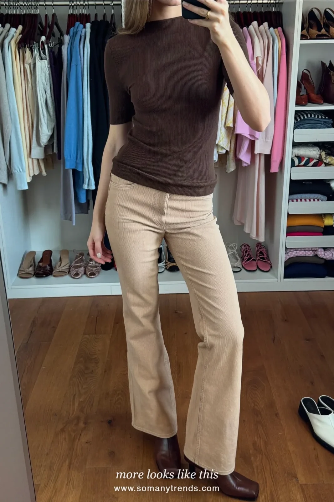 Woman in a chocolate knit top, beige flare pants and brown heeled boots taking a mirror selfie at home, outfit 24