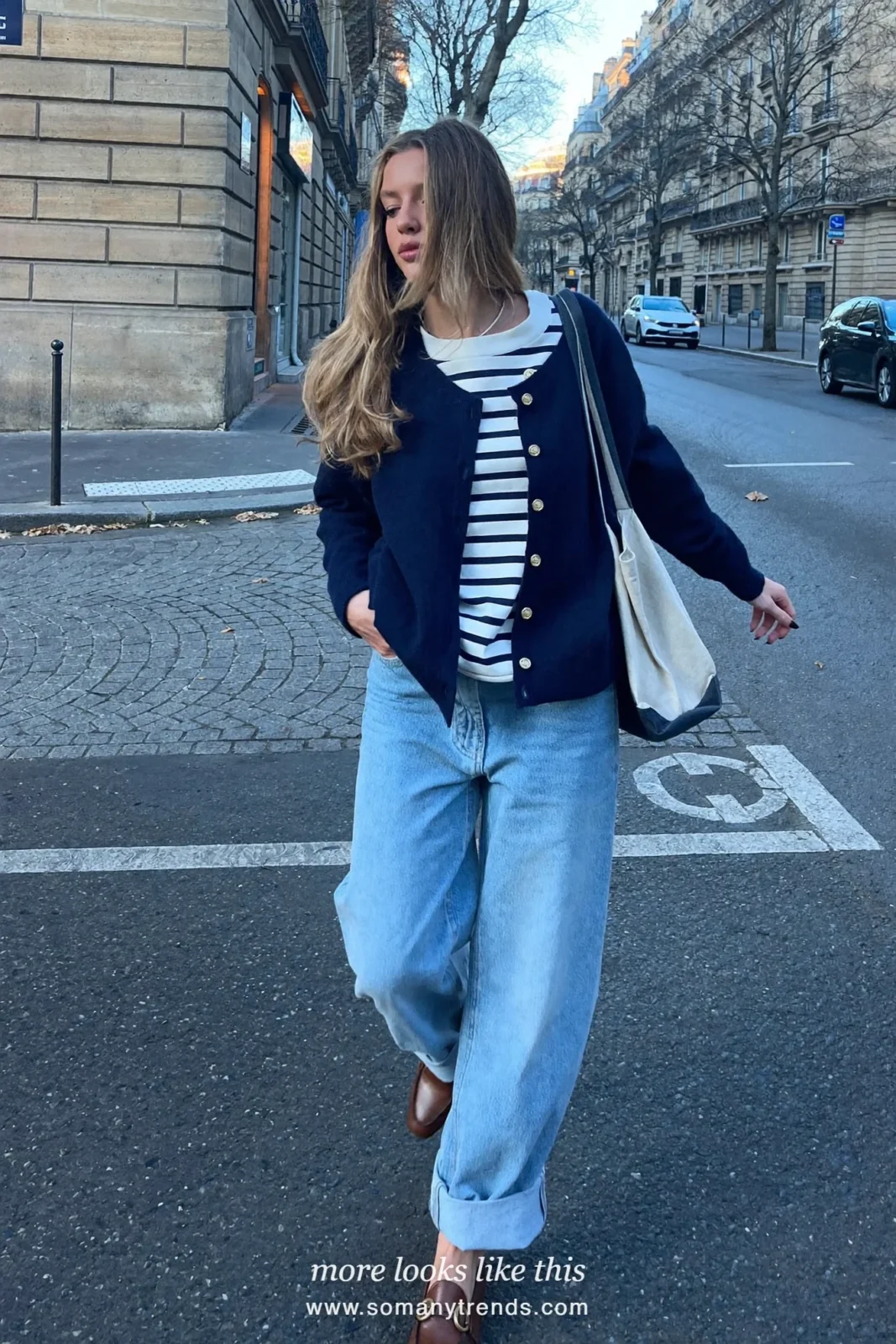 Woman in a navy cardigan with gold buttons, striped tee, light wide jeans and loafers in Paris, outfit 23