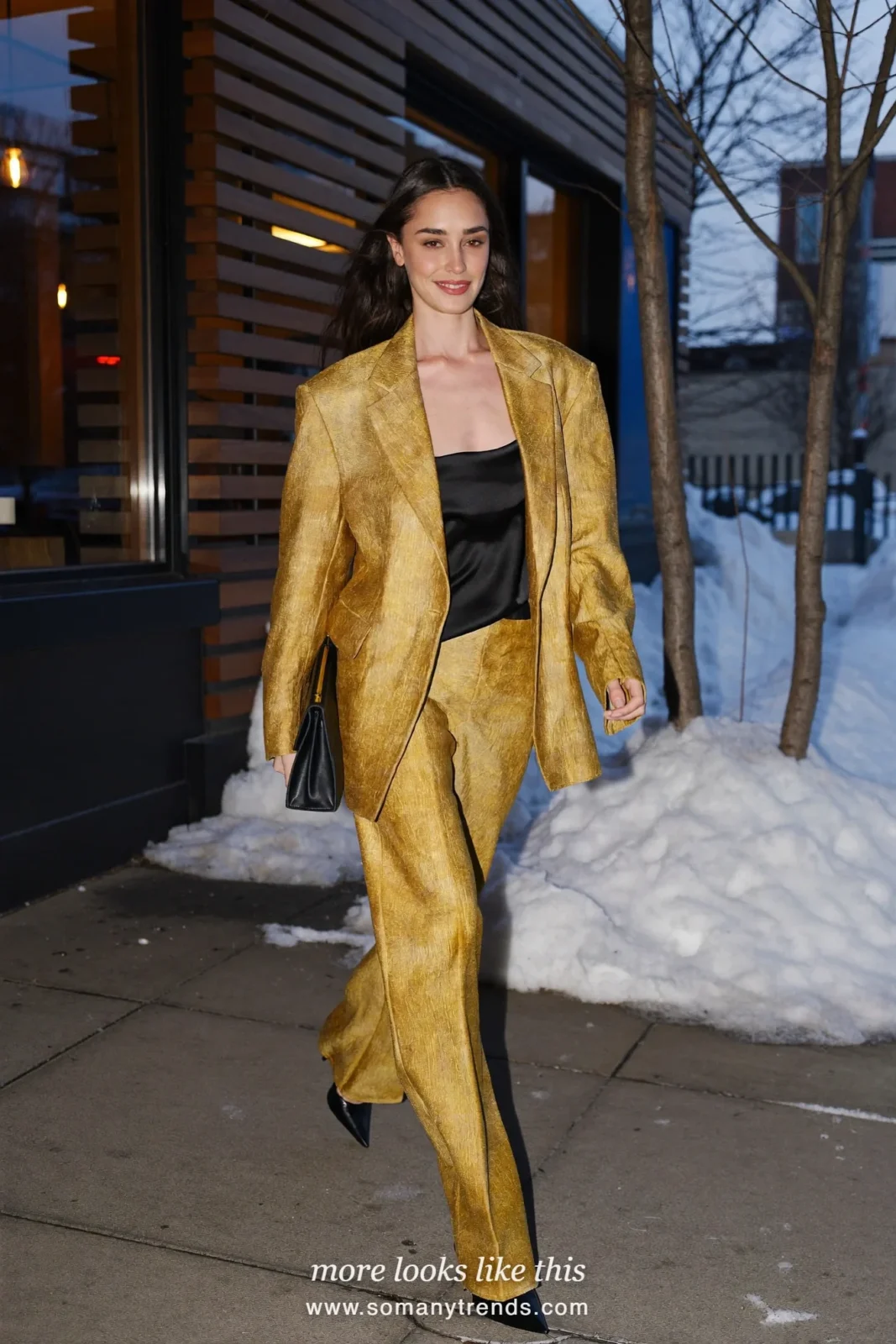 Woman in a mustard-gold trouser suit with a black tank and black pointed pumps outside a restaurant at dusk, outfit 2
