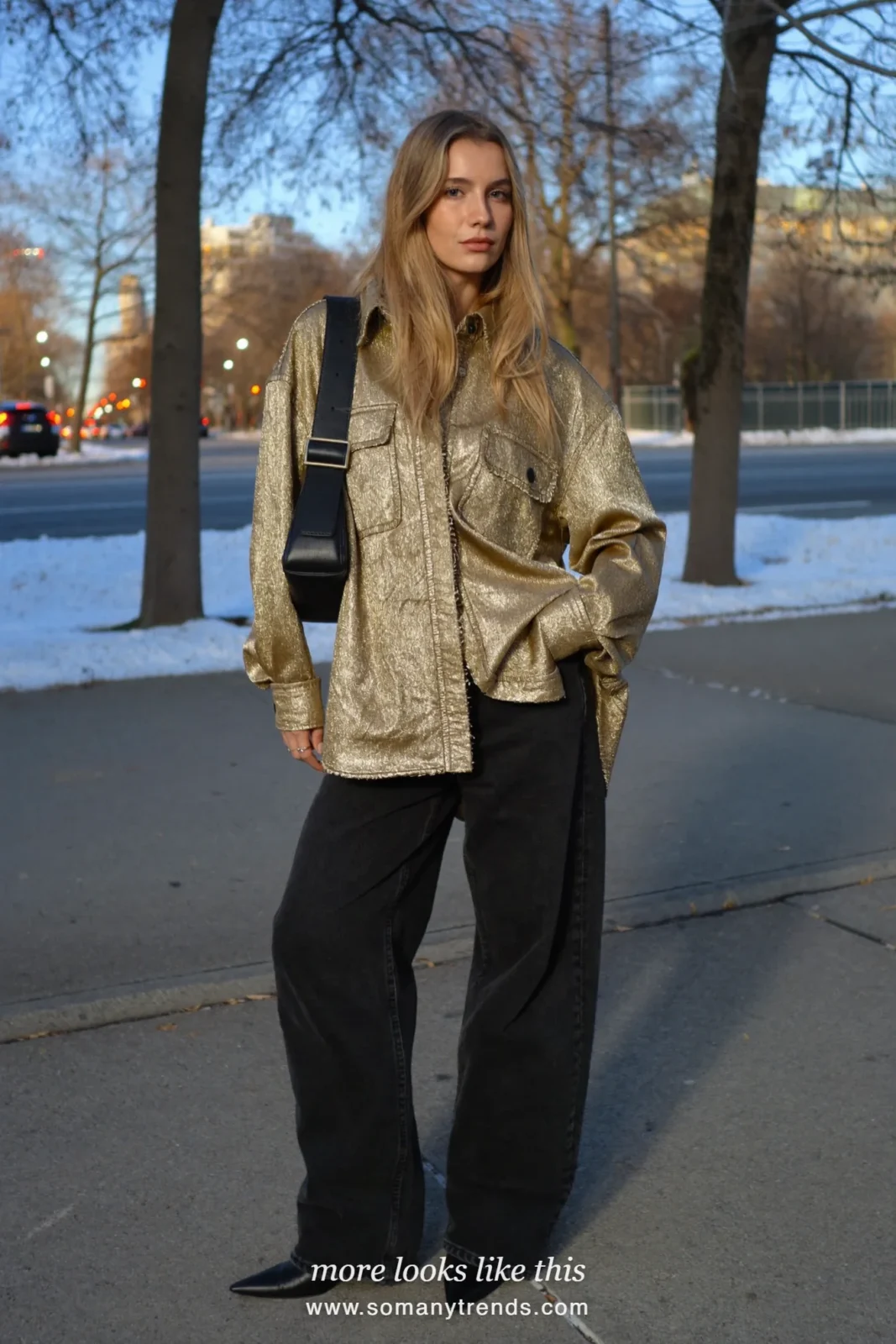 Woman in a gold metallic button-up shirt, black straight jeans and black pointed boots on a city street at dusk, outfit 7