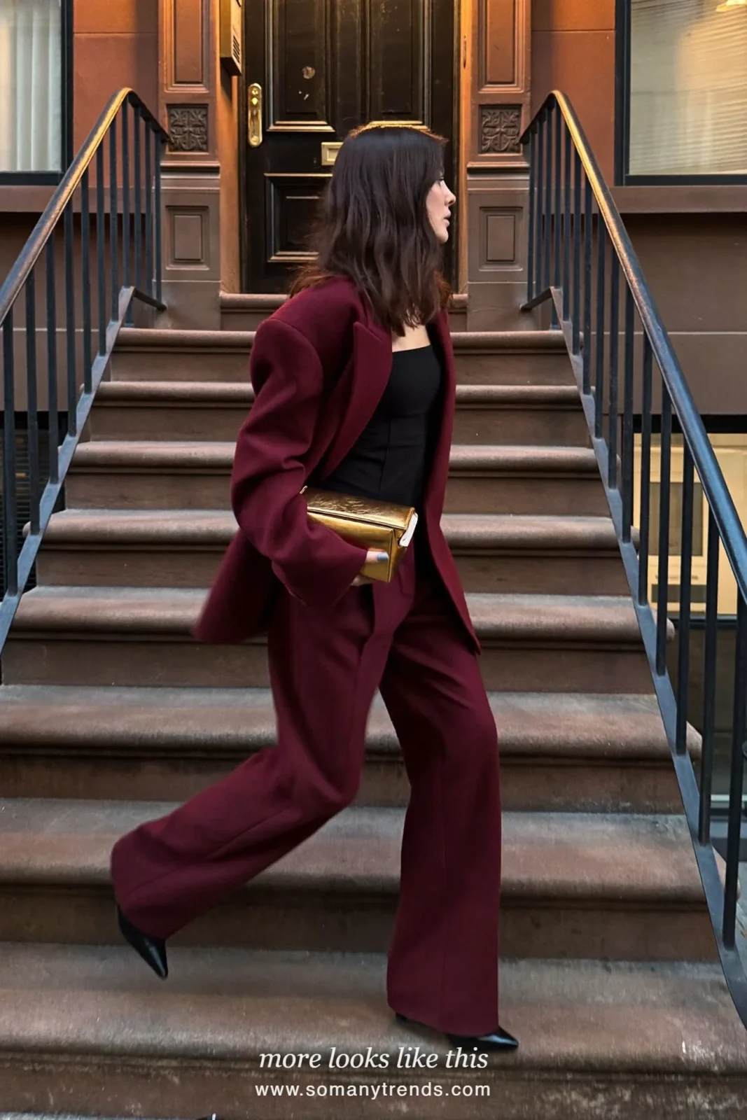 Woman in a burgundy wool suit, black top, black pointed boots and a gold clutch on a brownstone stoop, outfit 26