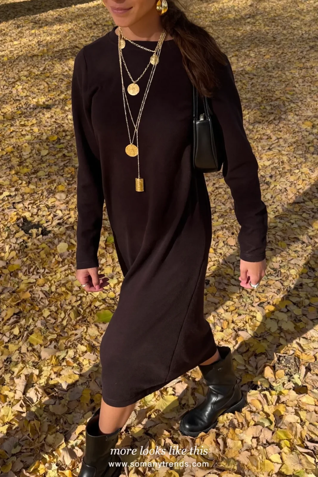 Woman in a black long-sleeve midi dress with chunky gold earrings and layered gold necklaces in a field of autumn leaves, outfit 27