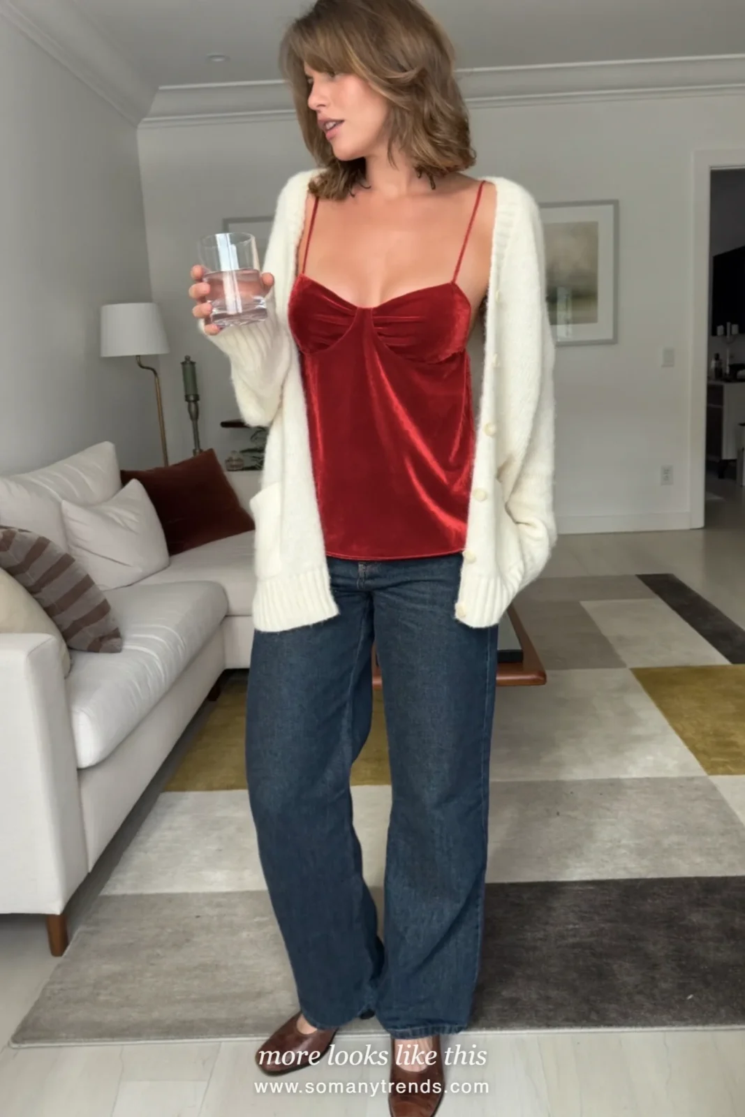 Woman in a red velvet cami, cream cardigan and dark straight jeans with ankle boots, house party outfit 21