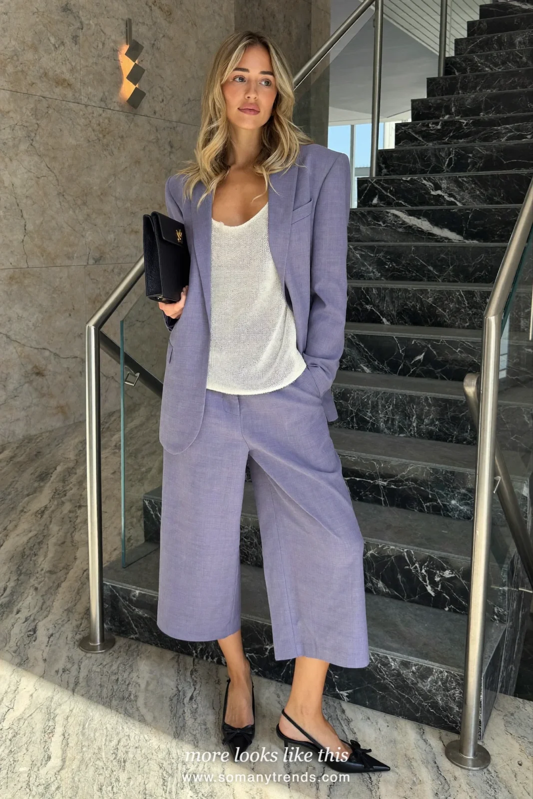 Woman in lavender-gray oversized trouser suit, ivory tank and black slingbacks on a spiral staircase, outfit 3