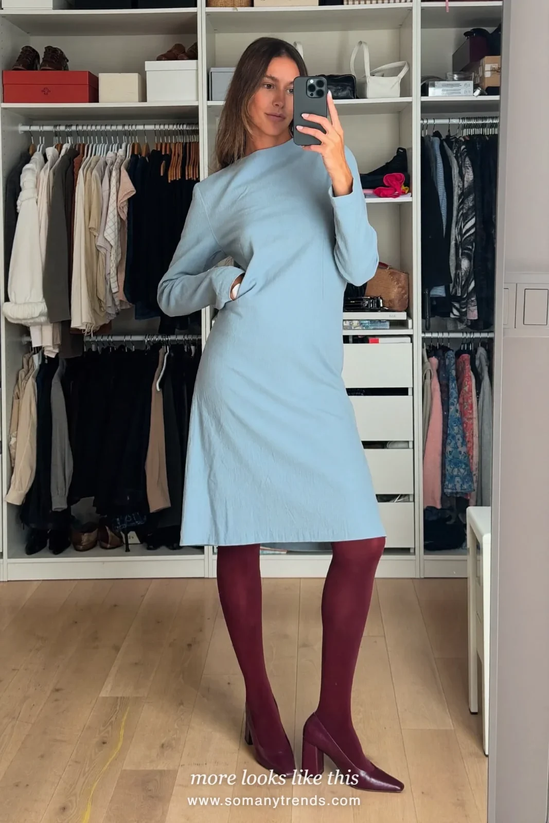 Woman in a burgundy wool coat over a baby blue midi dress with burgundy tights and burgundy pumps, outfit 18